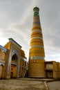 Khodja minaret and mosque madrasah in the historical center of Khiva with dark rain clouds, Uzbekistan