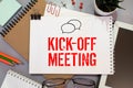 kickoff meeting, text on notepad sheet on brown background near magnifier and coffee cup Royalty Free Stock Photo