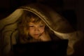 Kid alone at home. Kid boy lying on bed and surfing Internet on tablet in dark room. Child using tablet pc at night Royalty Free Stock Photo