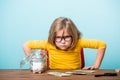 Kid boss. Angry little girl at the office desk with jar of money. Child in yellow bright clothes and glasses Royalty Free Stock Photo