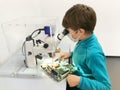 Kid boy conducts experiment with microscope in school lab. Curious inquisitive child learning physics and computer Royalty Free Stock Photo