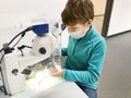 Kid boy conducts experiment with microscope in school lab. Curious inquisitive child learning physics and computer