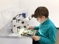 Kid boy conducts experiment with microscope in school lab. Curious inquisitive child learning physics and computer