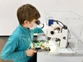 Kid boy conducts experiment with microscope in school lab. Curious inquisitive child learning physics and computer