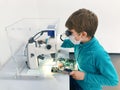 Kid boy conducts experiment with microscope in school lab. Curious inquisitive child learning physics and computer Royalty Free Stock Photo