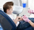 Kid boy in dental chair trains to clean teeth with a dummy mandibula jaw on background of dentist office