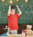 Kid boy in graduate cap ready to go to school, chalkboard on background. Child, pupil on smiling face near microscope Royalty Free Stock Photo