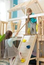 Kid boy helps child girl climb the rope up in playroom