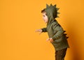 Kid boy in hoodie with dinosaurus spikes at his back and cowl act as a t-rex with his hands claws up and roars