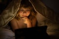 Kid boy lying on bed and surfing Internet on tablet in dark room. Child using tablet pc at night. Little kid in bed