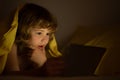 Kid boy lying on bed and surfing Internet on tablet in dark room. Child using tablet pc at night. Little kid in bed Royalty Free Stock Photo