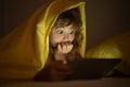 Kid boy lying on bed and surfing Internet on tablet in dark room. Child using tablet pc at night. Little kid in bed Royalty Free Stock Photo