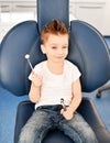 Kid boy in modern dental chair shows us a dental mirror and winks