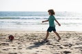 Kid boy play football on sand beach. Summer soccer on beach for children.