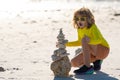 Kid boy playing with stones on the beach. Child play with pyramid of stones on the beach, sea seascape, rest and seaside Royalty Free Stock Photo