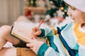 Kid boy in red Santa hat writing the letter and drawing to dear Santa at home. Child wish list. Dreams of a Christmas Royalty Free Stock Photo