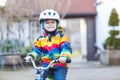 Kid boy in safety helmet and colorful raincoat riding bike, outd Royalty Free Stock Photo