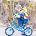 kid boy in safety helmet and colorful raincoat riding bike, outd Royalty Free Stock Photo