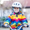 kid boy in safety helmet and colorful raincoat riding bike, outd Royalty Free Stock Photo