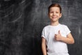 Kid boy showing thumb up gesture or liking on backdrop of black chalk board