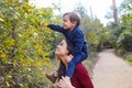 Kid boy sit on mother shoulders picking leave