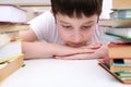 A kid boy sitting at the desk surrounded stacks of books, he is tired of learning and information