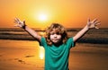 Kid boy on sunset beach, raised hands. Amazed surprised kids emotions.