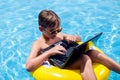 Kid boy using laptop in the swimming pool. Technology, summer and vacation concept Royalty Free Stock Photo