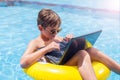 Kid boy using laptop in the swimming pool. Technology, summer and vacation concept Royalty Free Stock Photo
