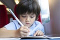 Kid boy wrinting on his book while traveling by the train, Child drawing or watching cartoon on teblet sitting by the window. Litt