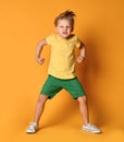 Kid boy in yellow t-shirt, green short and white sneakers is in a pose of angry monster demonstrating power and hisses with rage