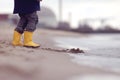 A kid in bright yellow rubber boots is playing at the surf zone of a sandy sea shore in front of a nuclear power plant Royalty Free Stock Photo