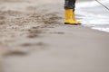 A kid in bright yellow rubber boots is standing at the surf zone of a sandy sea shore Royalty Free Stock Photo