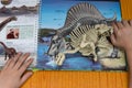 Kid checking a Spinosaurus skeleton against a book with details of the same dinosaur