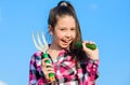 Kid cheerful gardener holds rake and cucumber blue sky background. Girl gardener with hand rake. Gardening and