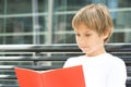 Kid doing homework, reading book textbook outdoors