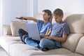 Kid doing homework task with laptop computer and brother turns on TV to watch educational program for pupils. Education Royalty Free Stock Photo