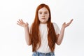 Kid dont know. Cute redhead little girl shrugging and raise hands up, look clueless and confused at camera, have no idea Royalty Free Stock Photo