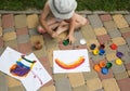 Kid draws a rainbow on paper with multi-colored paints, sitting barefoot on the paving slabs Royalty Free Stock Photo