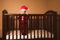 Kid dressed as Santa Claus stands in crib