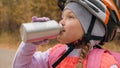 Kid drink water from an aluminum flask. One caucasian children rides bike road in autumn park. Little girl riding black Royalty Free Stock Photo
