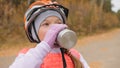 Kid drink water from an aluminum flask. One caucasian children rides bike road in autumn park. Little girl riding black orange mtb Royalty Free Stock Photo