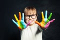 Kid enjoying his painting. Cute child girl with colorful hands on classroom blackboard background. Arts and creative education