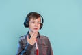 Kid enjoying music on his headphones, listening to music. Handsome young stylish kid in headphones standing against blue backgrou Royalty Free Stock Photo
