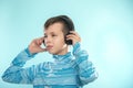 Kid enjoying music on his headphones, listening to music. Handsome young stylish kid in headphones standing against blue backgroun Royalty Free Stock Photo