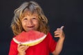 Kid face and watermelon, close up. Excited child boy eat watermelon. Kid is picking watermelon on gray background. Royalty Free Stock Photo