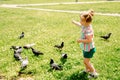 Kid is feeding pigeons in city park outdoors.Little baby girl running near doves. chasing pigeons, happy smiling child.Hot sunny Royalty Free Stock Photo
