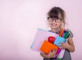 Kid gets ready for school. Schoolgirl holding many school supplies: pens, notebooks, scissors and apple. Back to school concept.