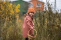 Kid girl in a brown coat and orange hat goes forward and turns to face. yellow leaves on the bushes. horizontal photo of a child