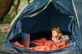 Kid girl in a campaign in a tent. Family summer vacation in nature. Children tourism. Child using laptop in the tent at the